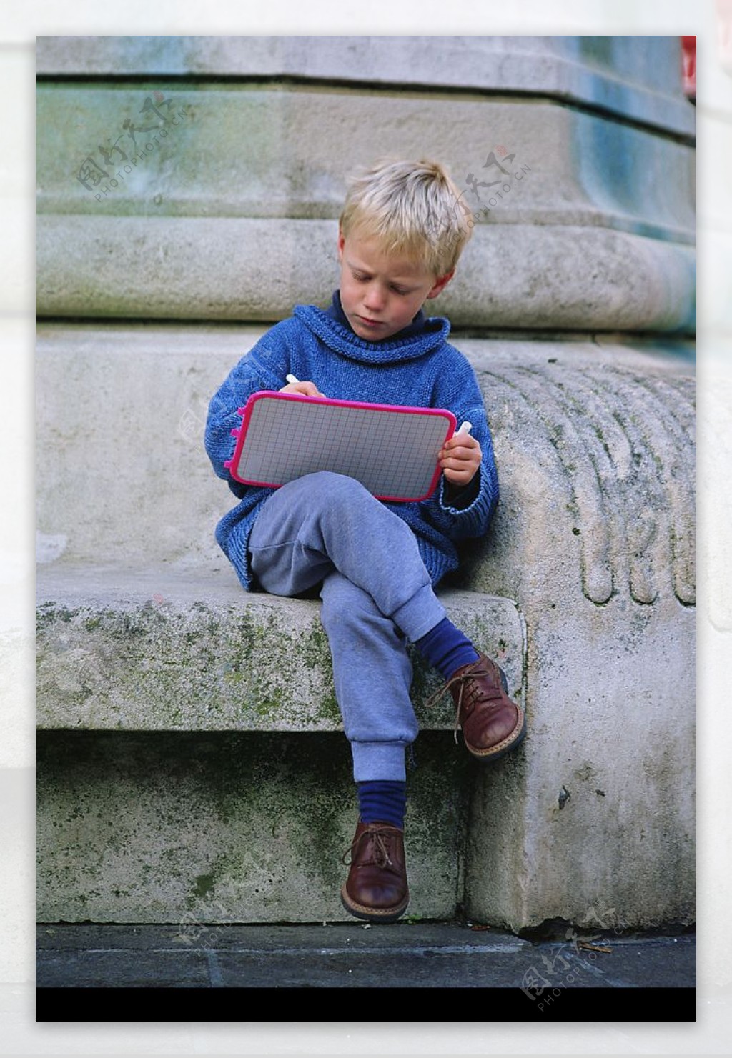 石柱旁坐着写字的外国男孩图片